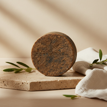 Load image into Gallery viewer, Jilyn Skincare African Black Soap 4oz bar styled with linen and botanicals on warm stone surface