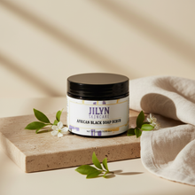 Load image into Gallery viewer, Jilyn Skincare African Black Soap Scrub 2.5oz jar styled with linen and botanicals on warm stone surface