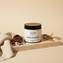 Load image into Gallery viewer, Jilyn Skincare Whipped Cocoa Butter 16oz black jar lifestyle photo on stone tray with cocoa props
