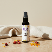 Load image into Gallery viewer, Jilyn Skincare Face Oil 2oz bottle styled with dried rosehip flowers and calendula petals on warm stone surface

